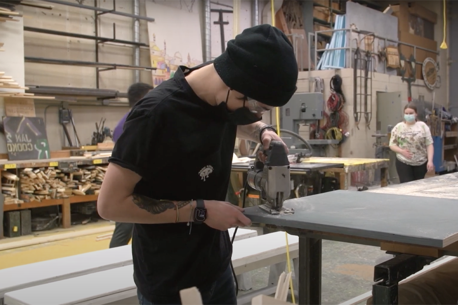 A student uses a drill to make backdrops for an upcoming opera.