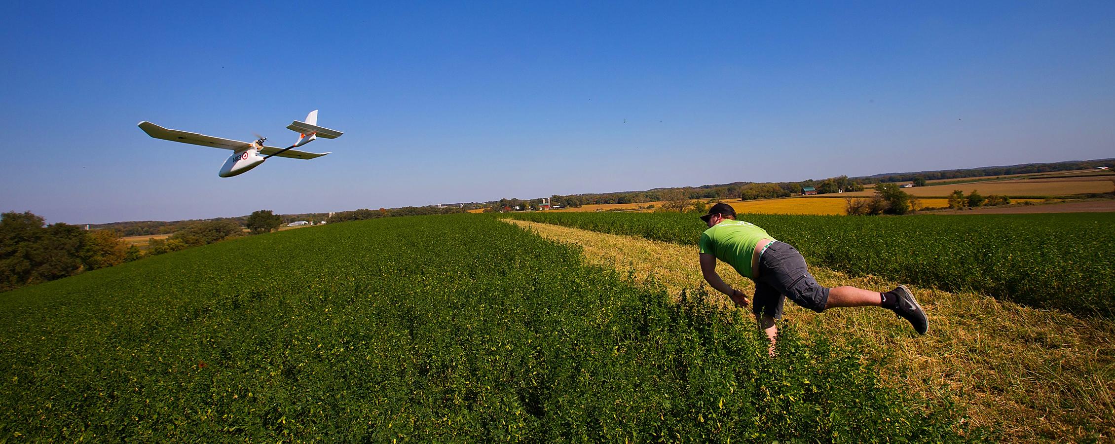 A student throws a mapping drone in a field.