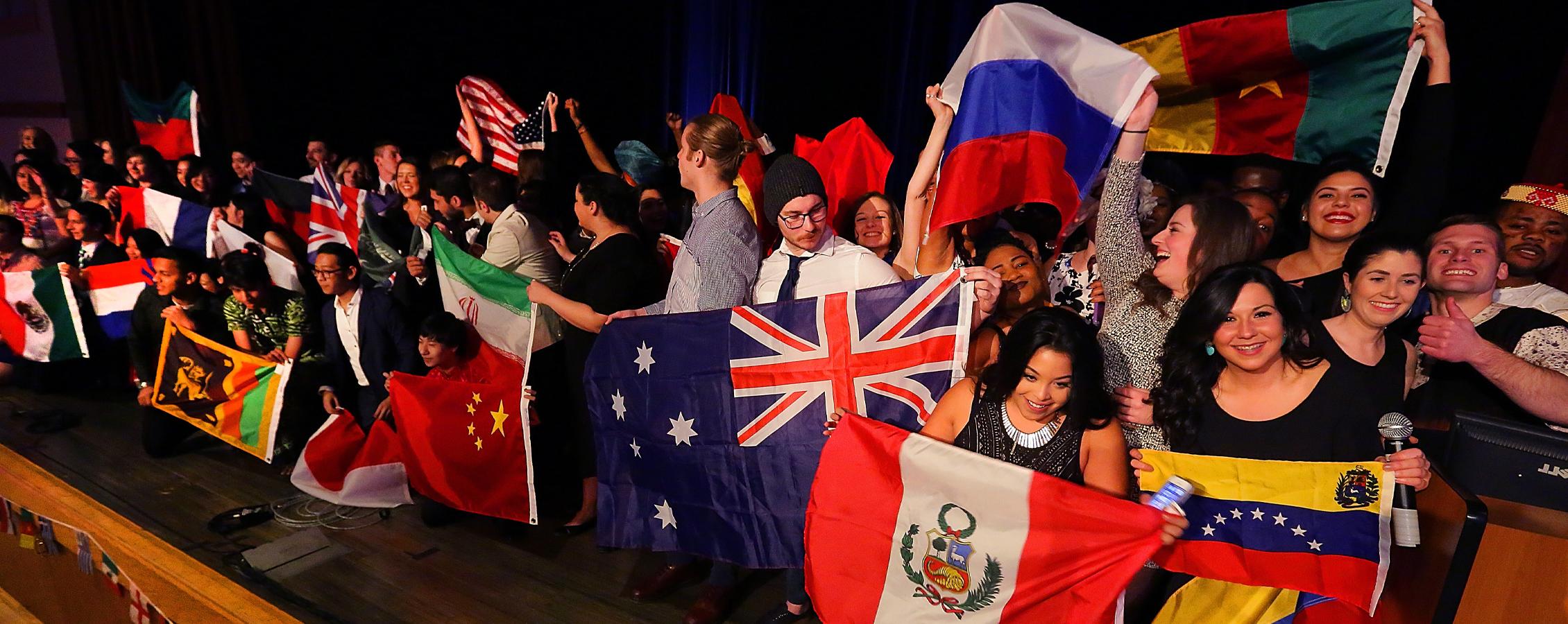 A large group of students hold flags from countries around the world.