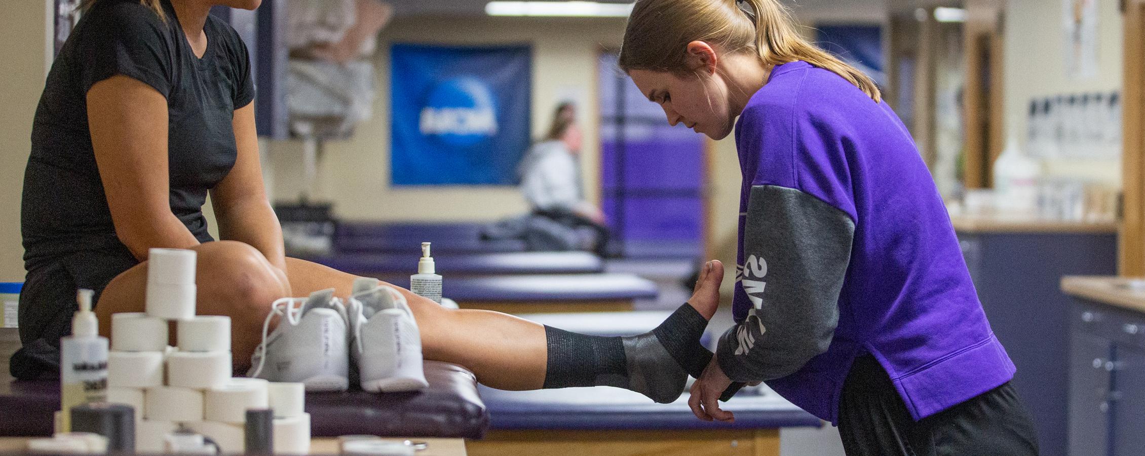 A student wraps the ankle of an athlete.