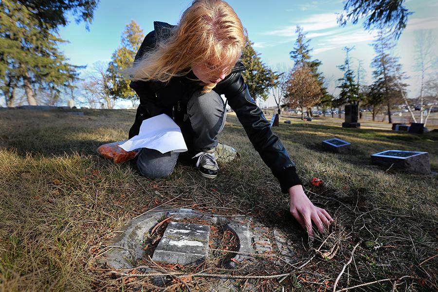 A student brushes away debris covering a grave marker.