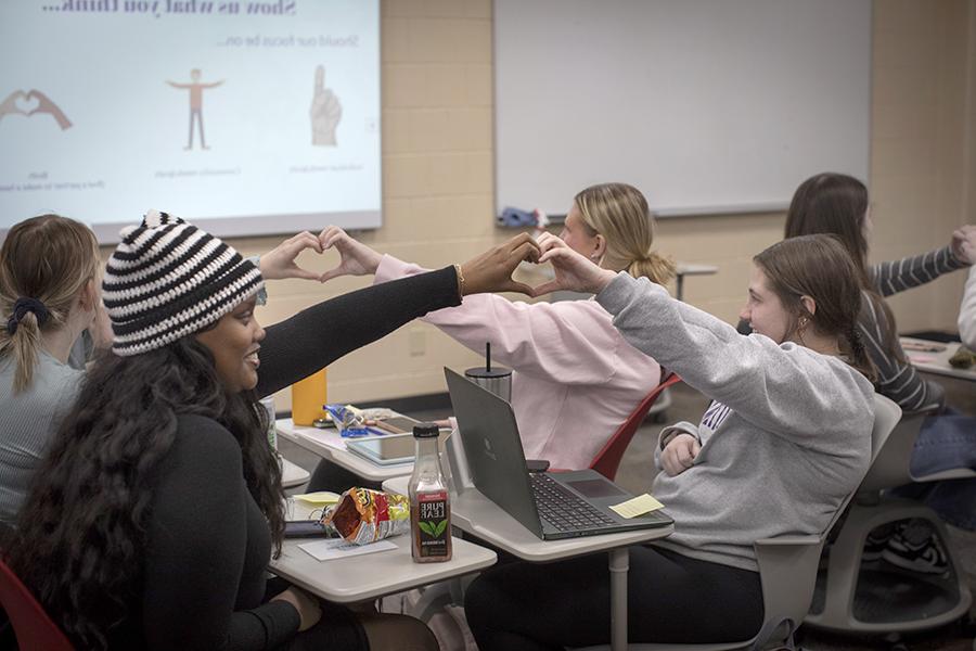 Students sit across form each other and connect their hands to make a heart.