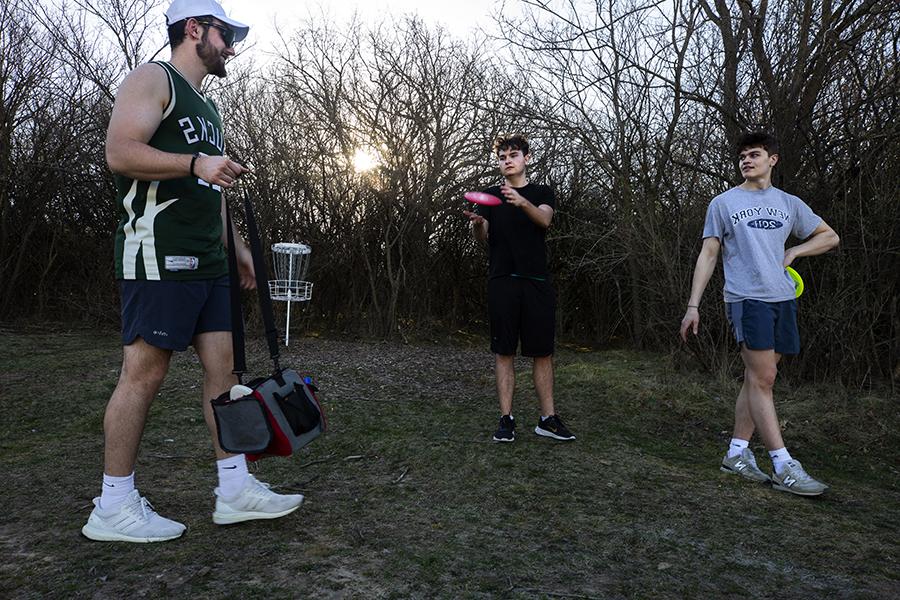 A group of students play frisbee golf during sunset.