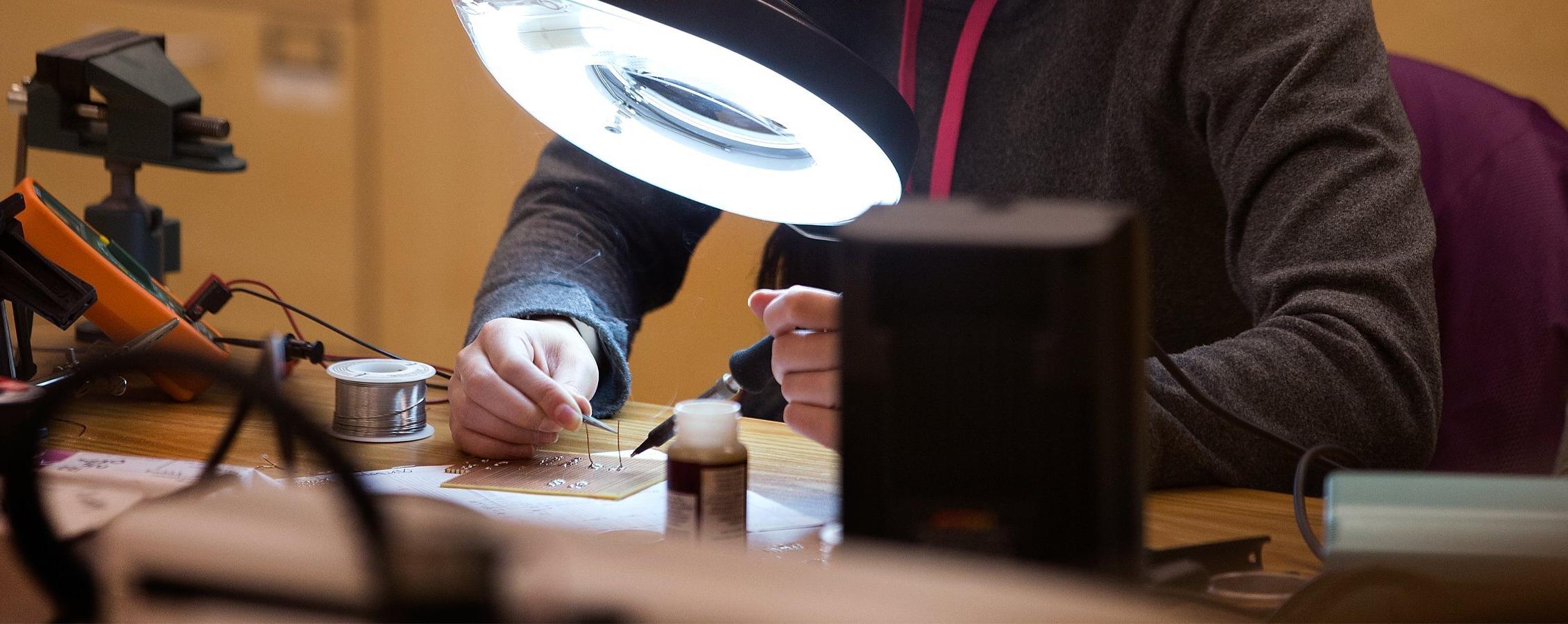 A student solders groups of micro wires under a large light.