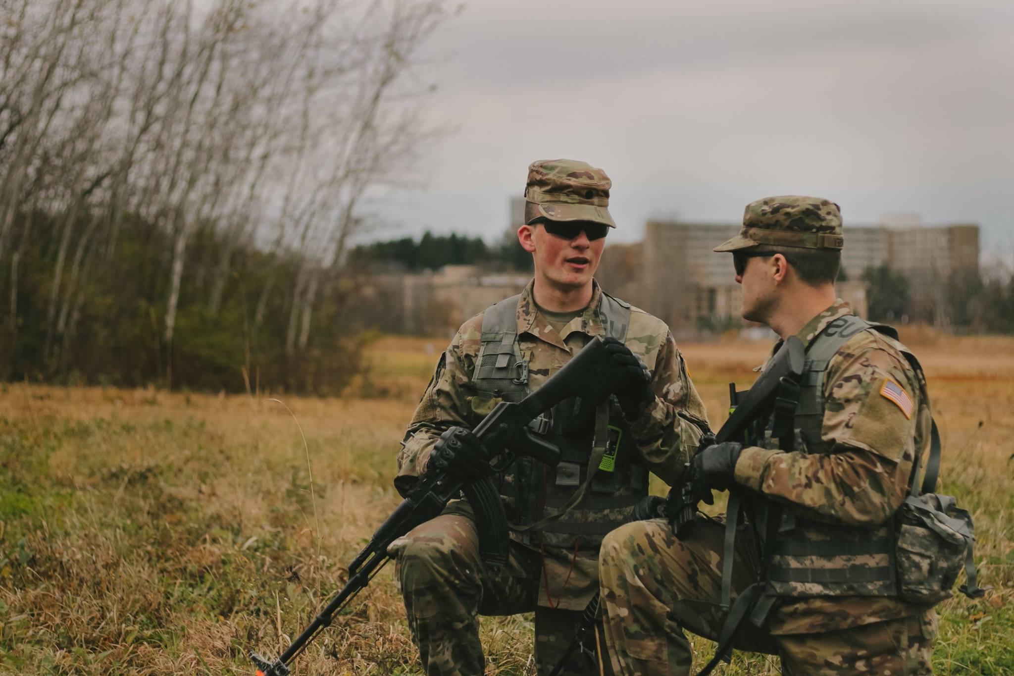 student in uniform kneeling in a field talking strategy