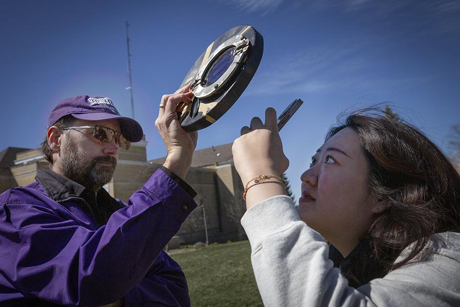 International student Bona Jeon photographs the sun through a solar filter held by an associate professor of physics.