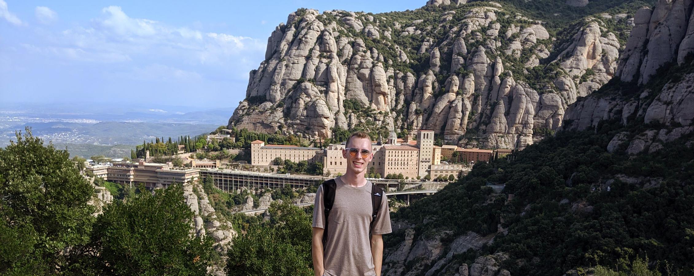 A person poses for a picture in front of a city built into a large mountain.