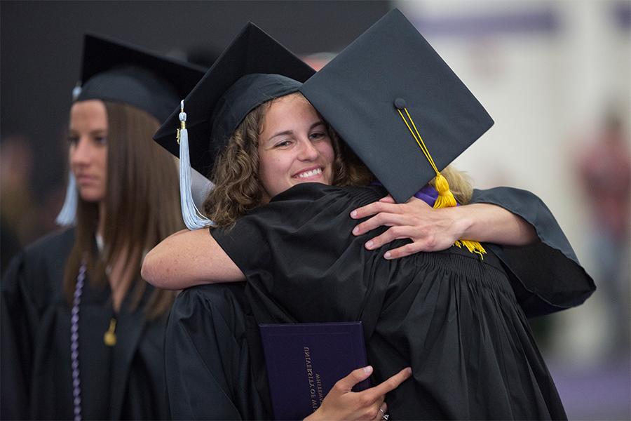 Kathleen Happel, left, hugs a student at graduation, both in cap and gown.