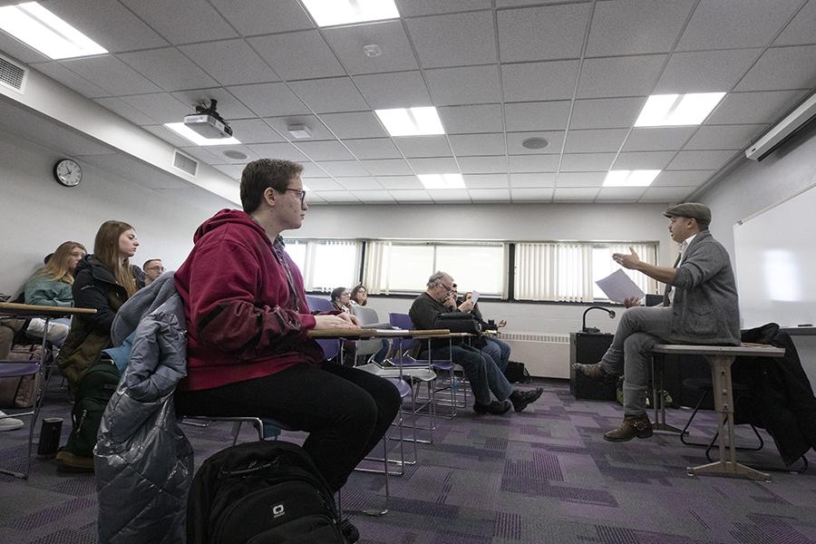 Nicholas Gulig sits on a table at the front of class and speaks to his students.