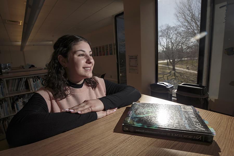 A student sits at a table with a book titled Neuroscience in front of her.