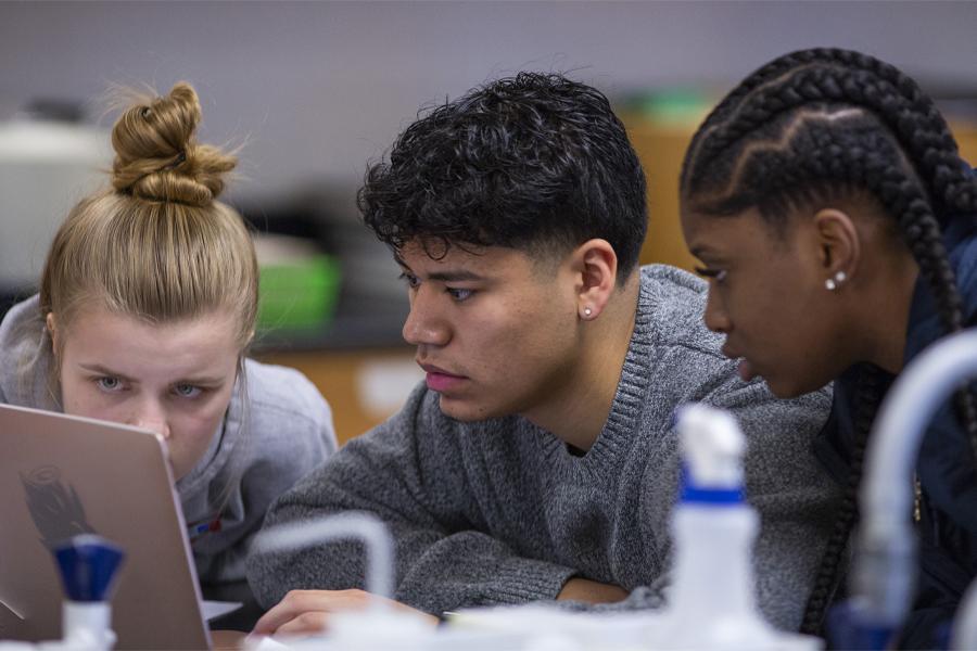 Three students work together on a laptop.