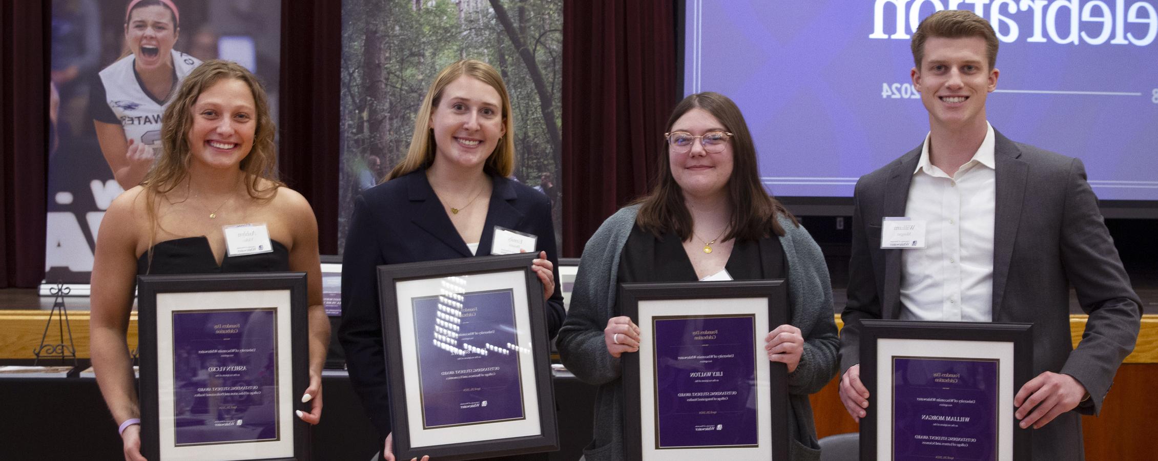 Four students pose together and each are holding a framed award.