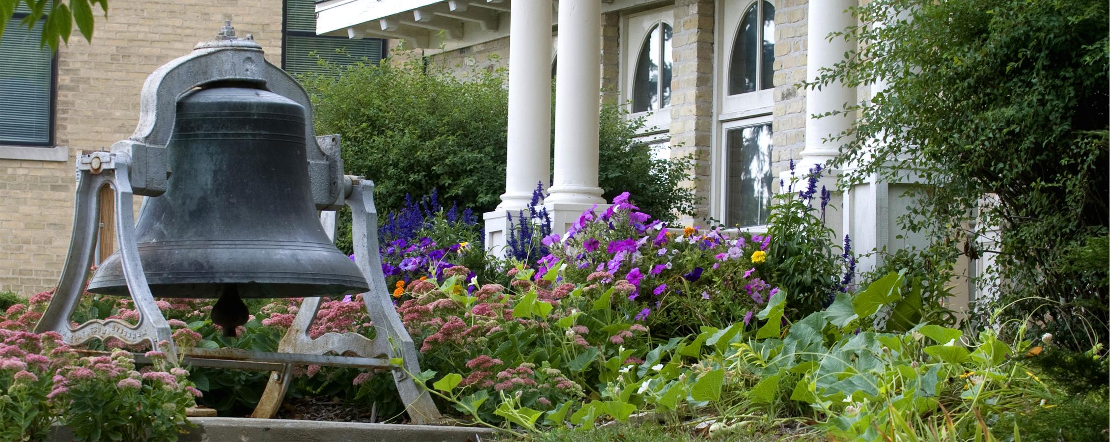 Bell tower outside of the Alumni Center surrounded by flowers.